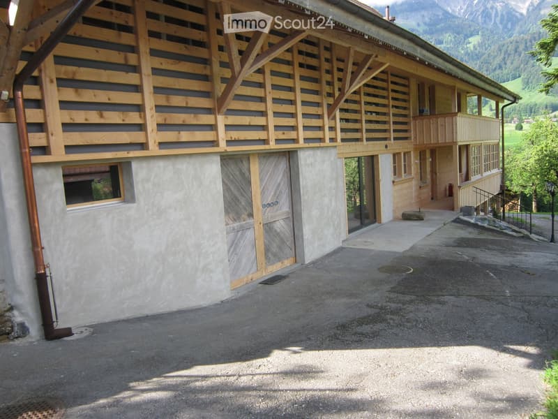 Building. Two-story wooden building with a balcony, garage, and scenic mountain backdrop.