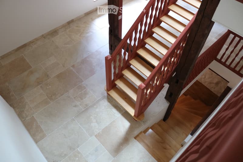 Corridor / Hallway. A staircase with wooden steps and a red wooden railing, leading to an upper level. The lower level has beige tiled flooring, while the upper level features wooden flooring.