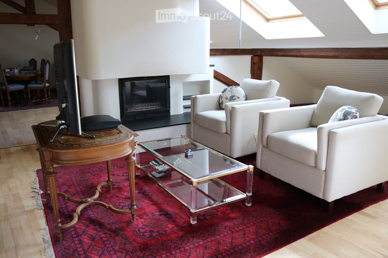 Living Room. Living room with a fireplace, two white armchairs, a glass coffee table, a television on a wooden stand, and a dining area with chairs and a table in the background.
