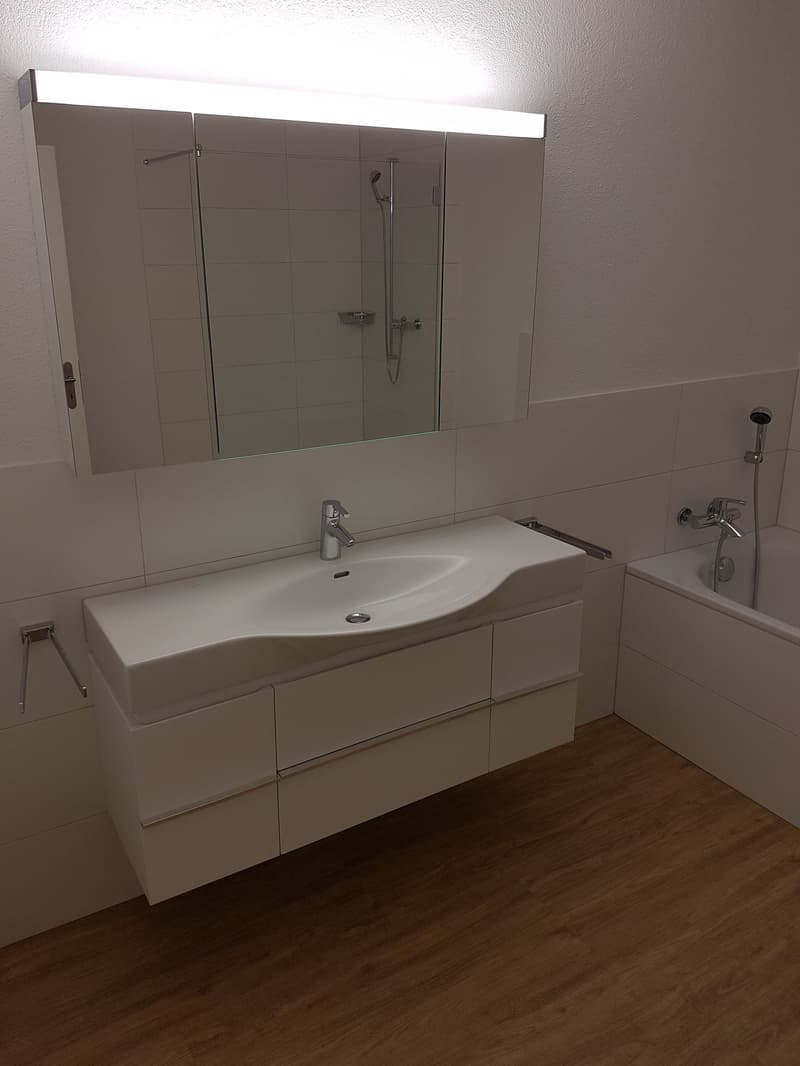 Bathroom. Modern bathroom with white sink, mirror, and cabinets. Wooden floor and white tiles.