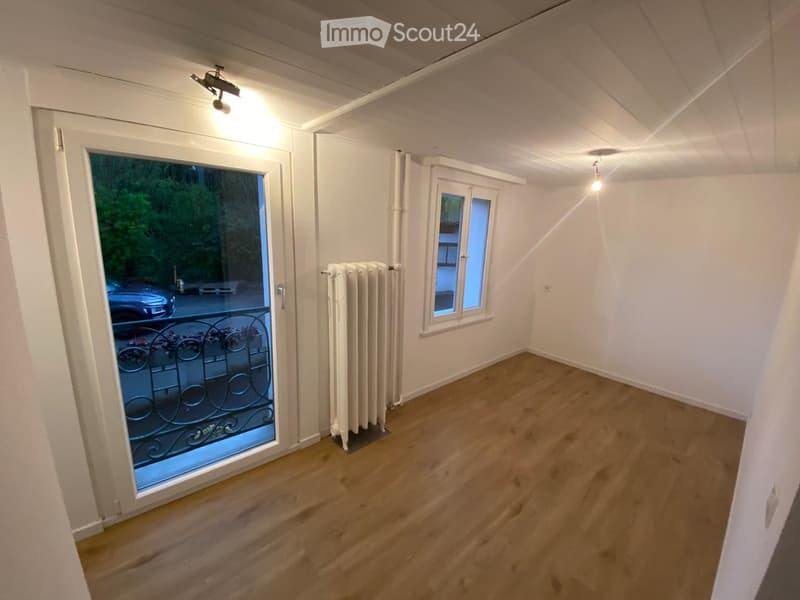 Unfurnished Room. Empty room with wooden flooring, white walls, a radiator, and a large window with a view of a balcony and outdoor area.
