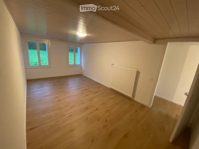 Unfurnished Room. Empty room with wooden flooring, white walls, and a radiator. Natural light from windows illuminates the space.