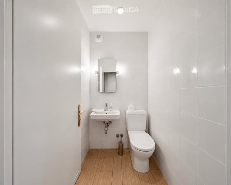 Bathroom. Modern, compact bathroom with white tiled walls, wooden floor, sink, toilet, mirror, and toilet paper holder.