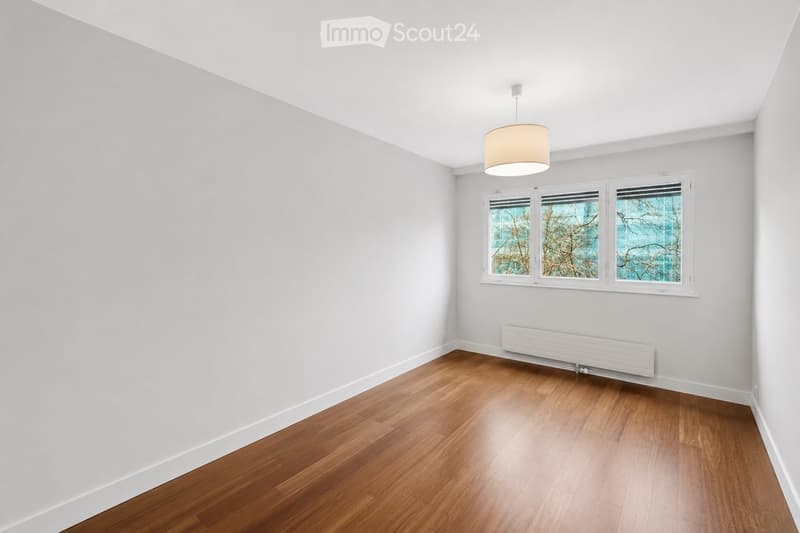 Unfurnished Room. Empty room with light grey walls, wooden flooring, and a single hanging light fixture. Three windows with frosted glass panels are visible on one wall.