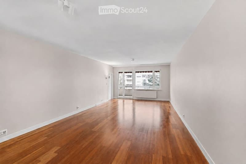 Unfurnished Room. Empty room with wooden flooring, light-colored walls, and large windows with a view of the outside. No furniture or equipment is present.
