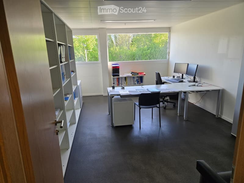 Furnished Room. Office space with two desks, chairs, computer screens, keyboards, shelves with books, and a telephone.
