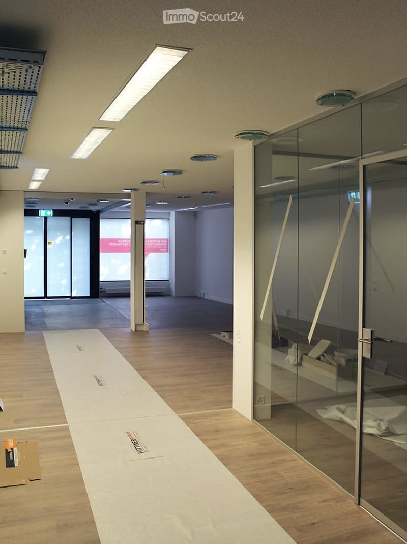 Empty hallway with wooden flooring, glass partitions, and recessed lighting. No furniture or equipment visible.