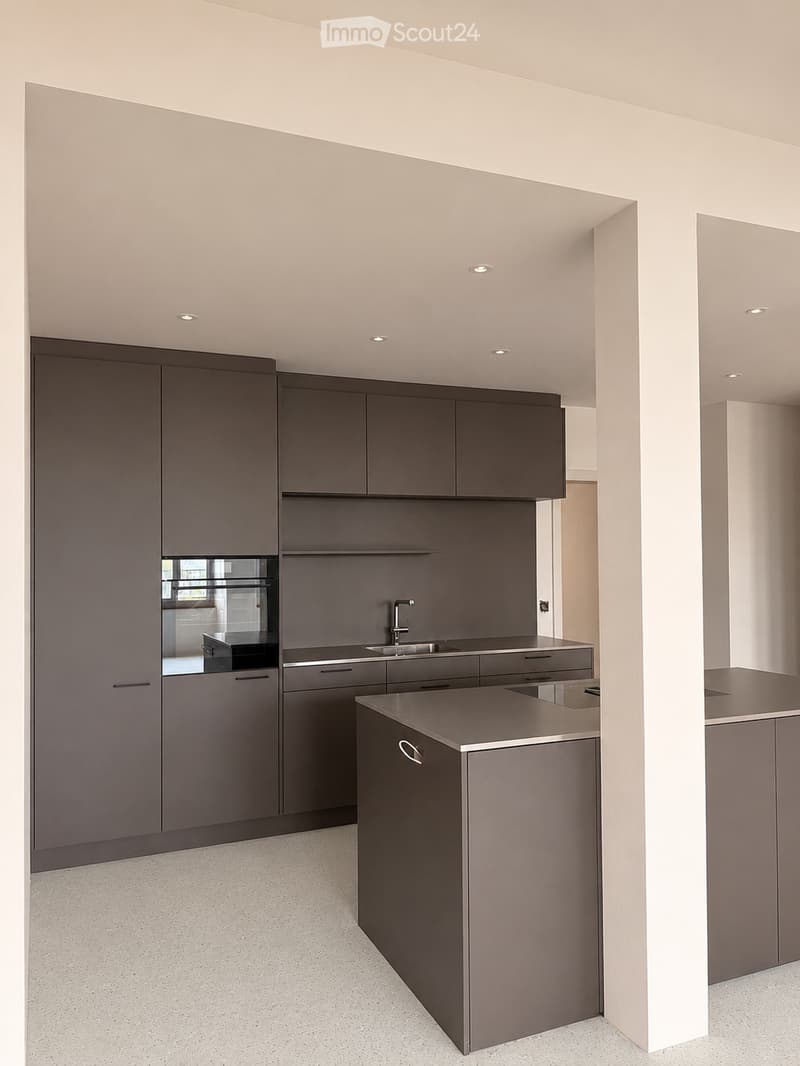 Kitchen. Modern kitchen with dark grey cabinets, a central island, and a sink with a faucet. The space features recessed lighting and a clean, minimalist design.