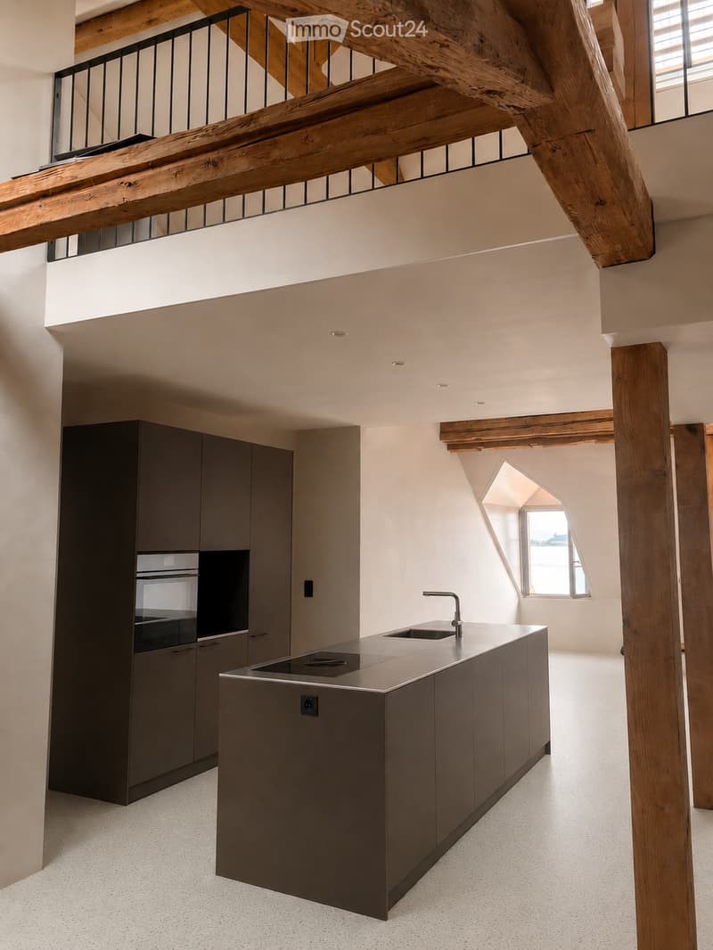 Kitchen. Modern kitchen with a central island, stainless steel sink, faucet, built-in oven, and dark grey cabinets. Exposed wooden beams and a balcony overlook the space.