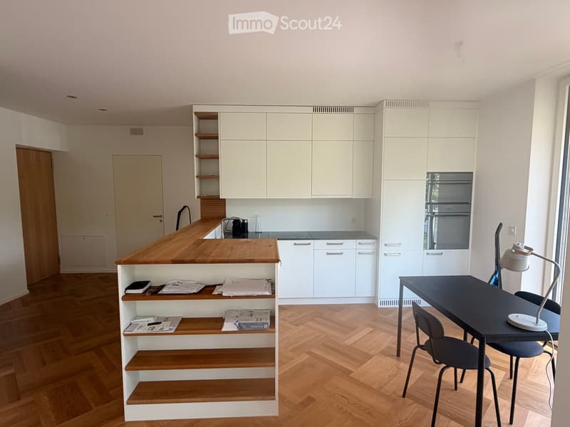 Furnished Room. Modern kitchen with white cabinets, wooden countertop, built-in oven, and a small dining area with a black table and chairs.