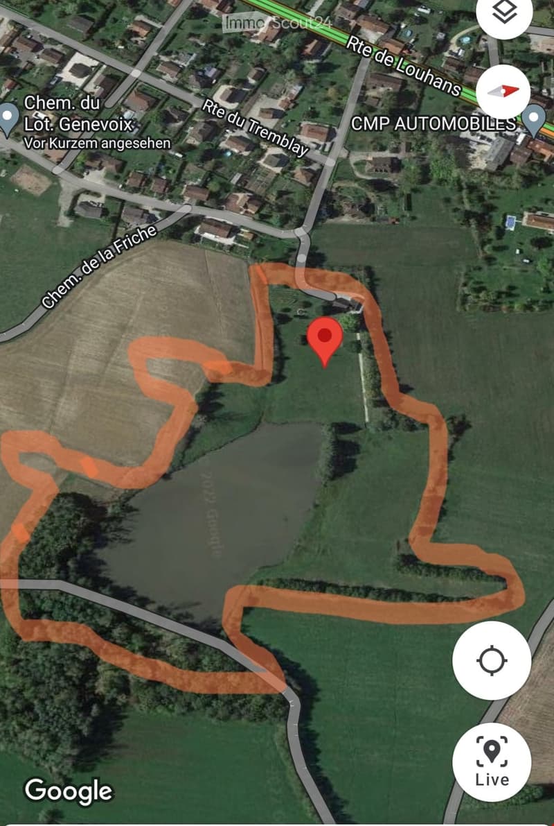 Building. Aerial view of a rural area showing a building surrounded by green fields and a small water body. Roads and other buildings are visible in the background.