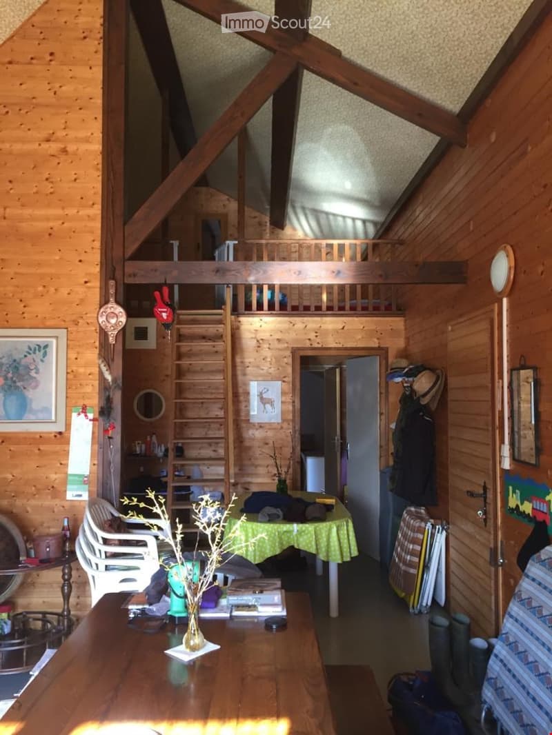 Furnished Room. Cozy wooden interior with a raised loft area, a small table with chairs, a vase on a wooden table, and various decorative items.