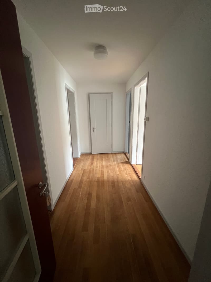 Empty hallway with wooden flooring, white walls, and several doors and windows.