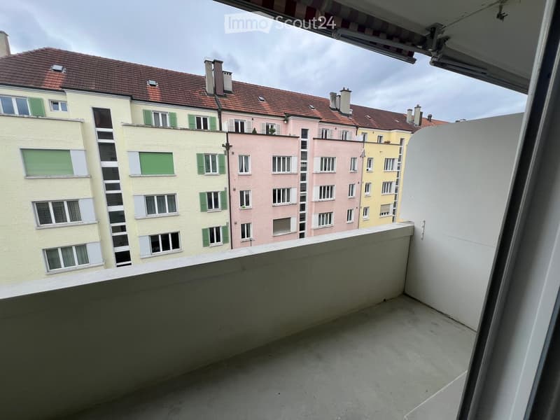 Empty balcony overlooking a row of colorful residential buildings with green shutters and red-tiled roofs.