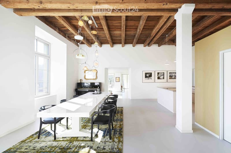 Furnished Room. Open-plan dining and living area with exposed wooden beams, white dining table with black chairs, piano, and modern pendant lights.