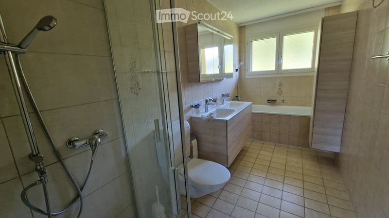 Modern bathroom with beige tiles, a glass-enclosed shower, a toilet, a sink with a mirror, and a bathtub.