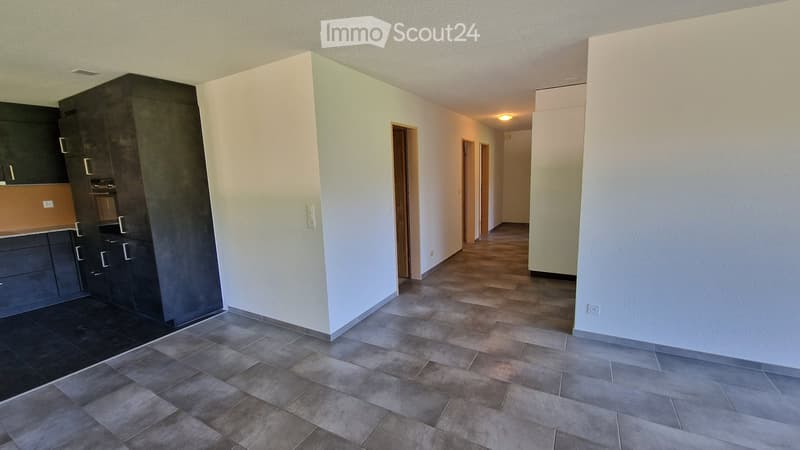 Empty hallway with tiled flooring, white walls, and a modern kitchen area visible on the left side.