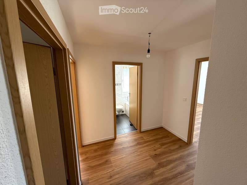 Wooden floors, white walls, light fixture, door leading to bathroom