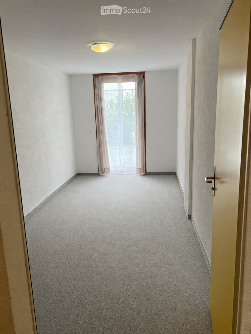 Unfurnished Room. Empty hallway with carpeted floor, white walls, a single ceiling light, and a window with curtains at the end.