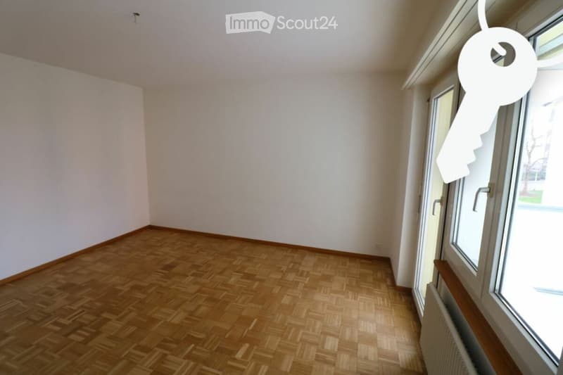 Empty room with wooden flooring and white walls, featuring a window with a key hanging on it.