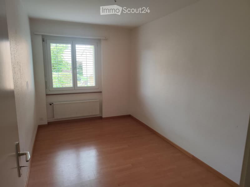 Empty room with wooden flooring, white walls, a window with blinds, and a radiator below it.