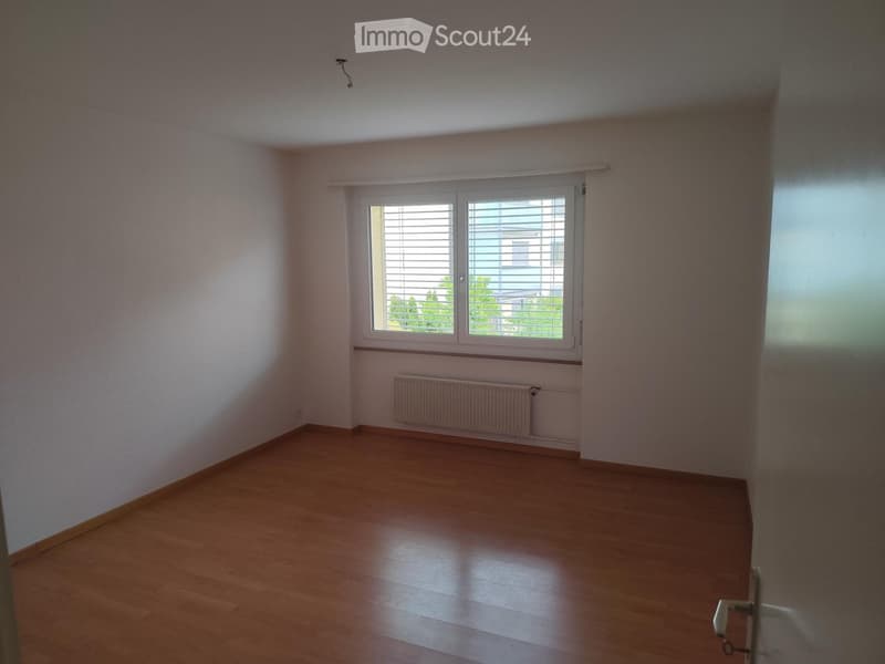Empty room with wooden flooring, white walls, a window with blinds, and a radiator under the window.