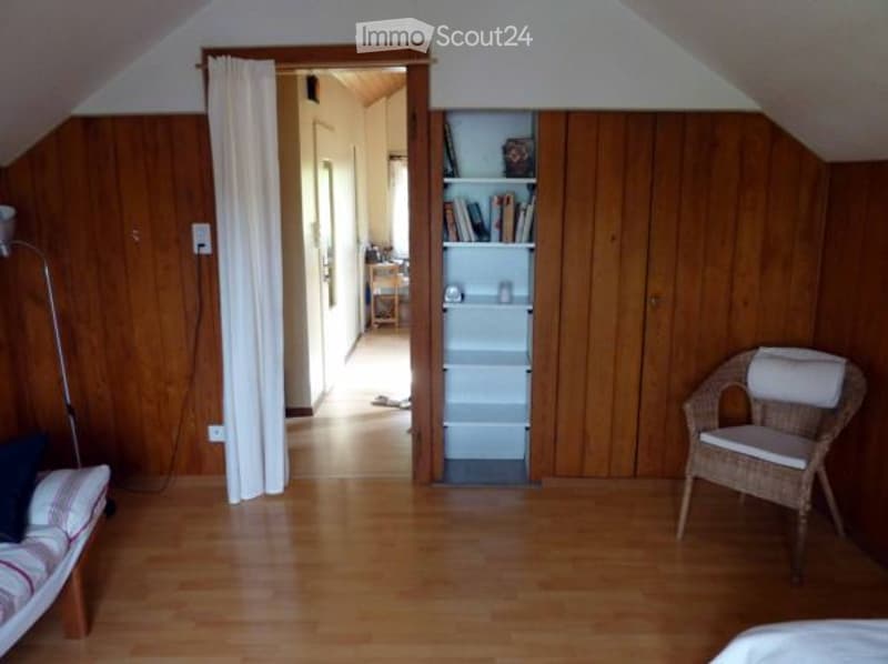 Attic bedroom with wood paneled walls, hardwood floor, bookshelf, and wicker chair