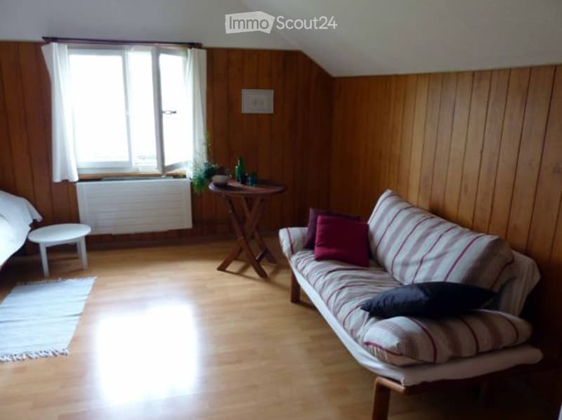 Cozy living room with wooden paneled walls, large windows, a striped sofa, a small table, and a rug on the hardwood floor.