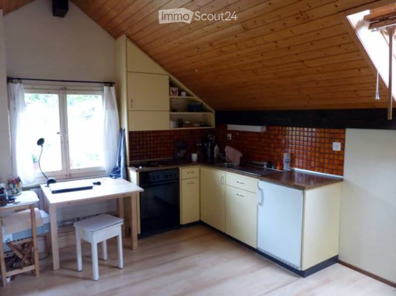 Attic kitchen with wooden ceiling, white cabinets, tiled backsplash, and a dishwasher. There is a small dining table and chairs in the corner.