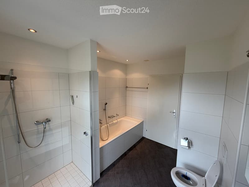 Modern bathroom with a bathtub, toilet, shower, and glass shower enclosure. Features white tiles, a dark floor, and built-in storage cabinets.