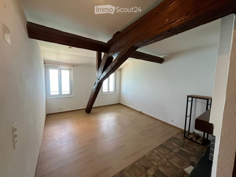 Empty room with wooden floor, exposed wooden beams, white walls, and two windows. No furniture or equipment present.