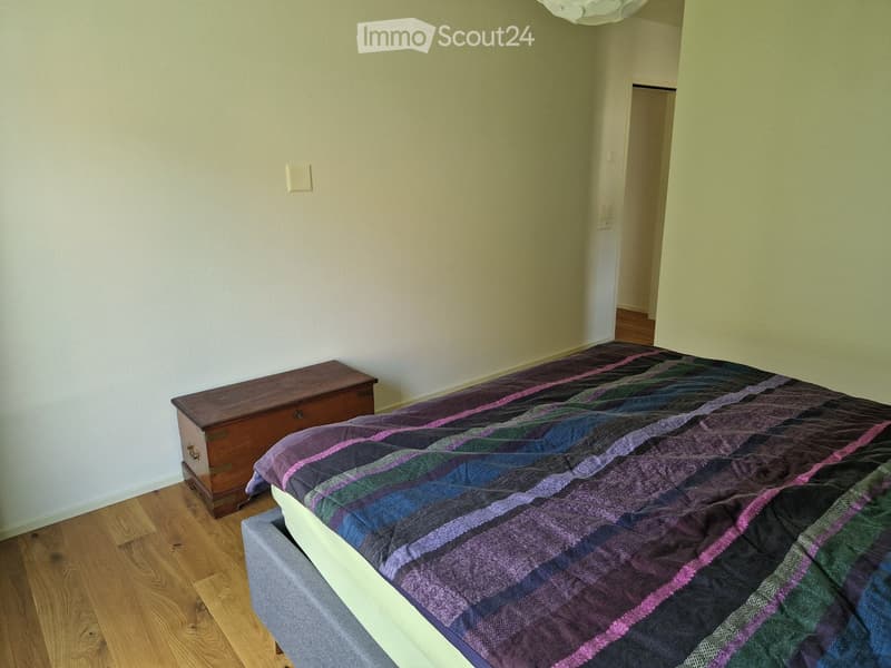 Bedroom with bed, wooden chest of drawers, white walls, wooden floor