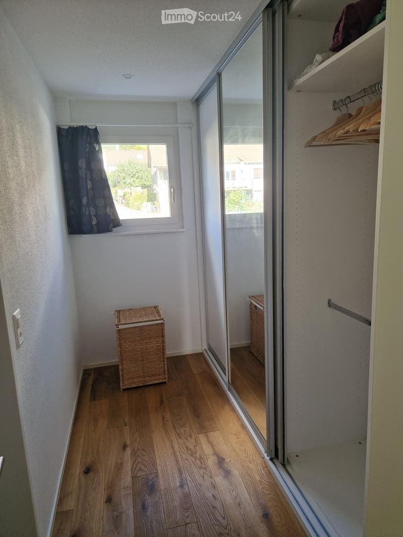 hallway with wooden flooring, large mirror, closet with hanging clothes, small basket