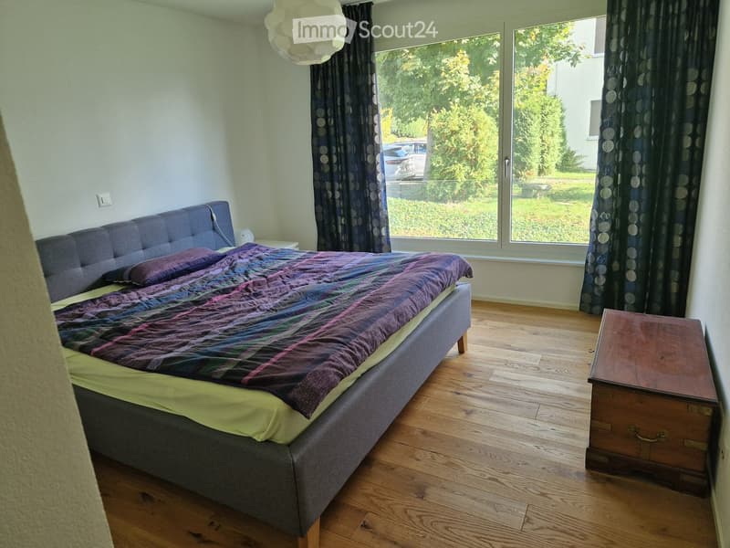 bedroom with bed, bedside tables, wooden chest, wooden floor, large windows, view of the outside