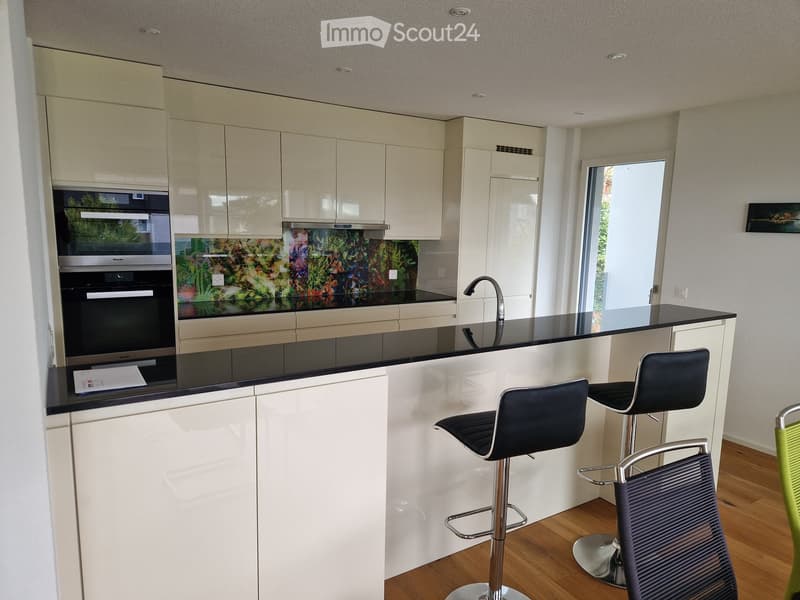modern kitchen with black countertops, white cabinets, double oven, sink, island, stools, and dishwasher
