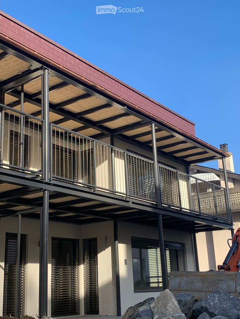 Modern two-story building with a covered balcony and metal railing, featuring large windows and a red-tiled roof.