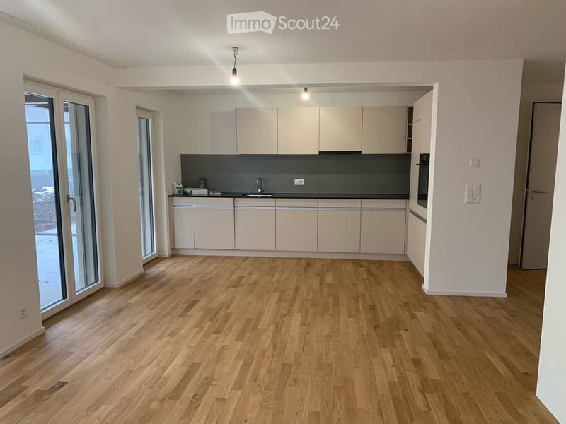 Modern kitchen with light wooden cabinets, a dark backsplash, and a wooden floor. Features a sink, faucet, and an oven.