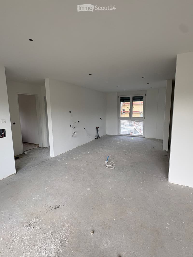 Empty room with concrete floor, white walls, and a large window with a view of a construction site.