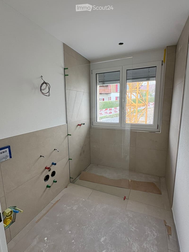 Empty bathroom with tiled walls and floor, glass shower enclosure, and visible construction materials and tools.