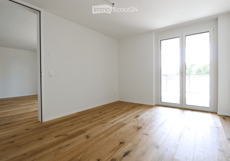 Empty room with light wooden flooring, white walls, and a large sliding glass door leading to a balcony.