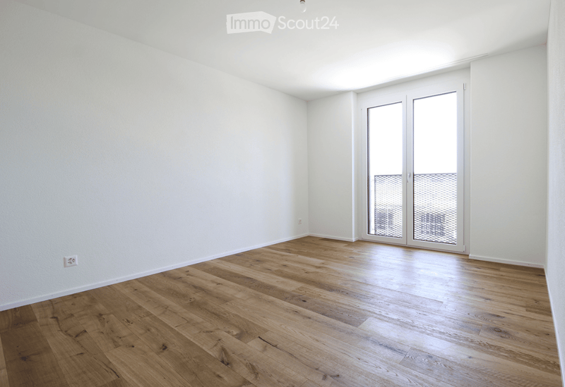 Empty room with light wooden flooring and white walls, featuring a set of glass doors leading outside.