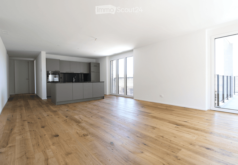 Open-plan kitchen and living area with light wooden flooring, grey cabinets, and a central island.