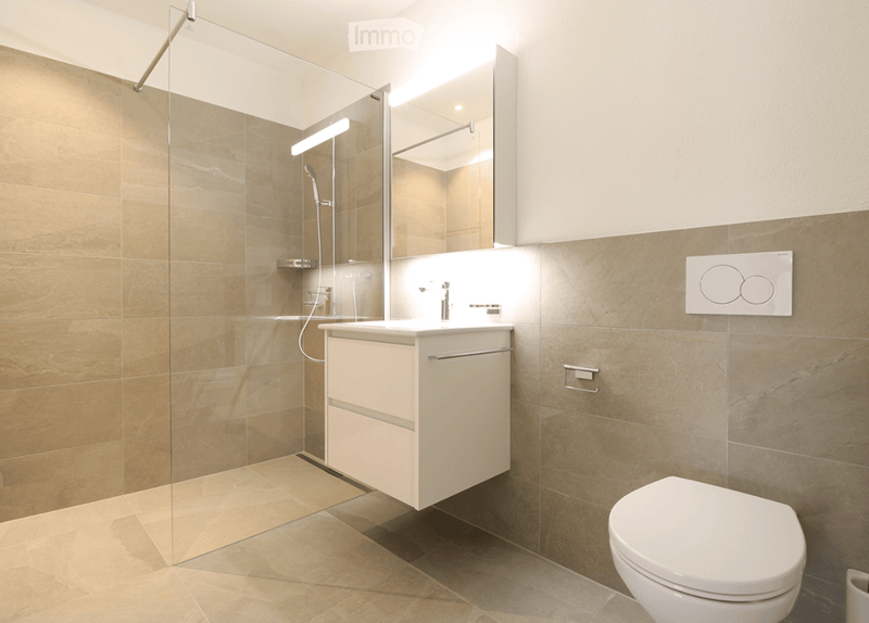 Modern bathroom with beige tiles, a white sink cabinet, a toilet, a glass-enclosed shower, and a large mirror above the sink.