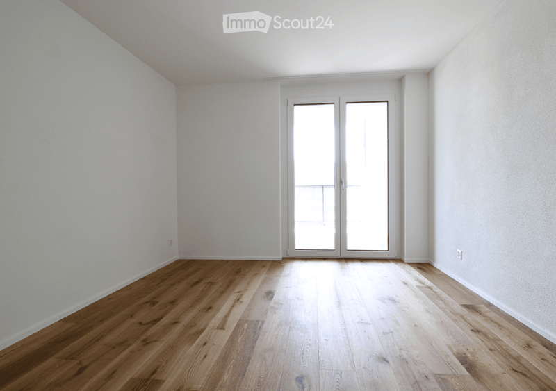 Empty room with light-colored wooden flooring and white walls, featuring a large glass door leading outside.