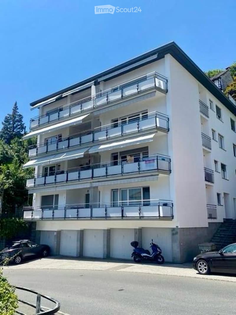 Modern multi-story apartment building with balconies, garage, and parking area.