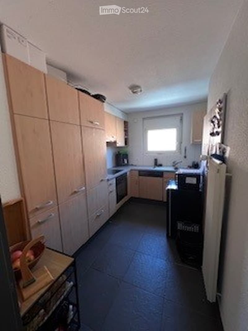Modern kitchen with light wooden cabinets, stainless steel appliances, dark tiled floor, and a window above the sink.
