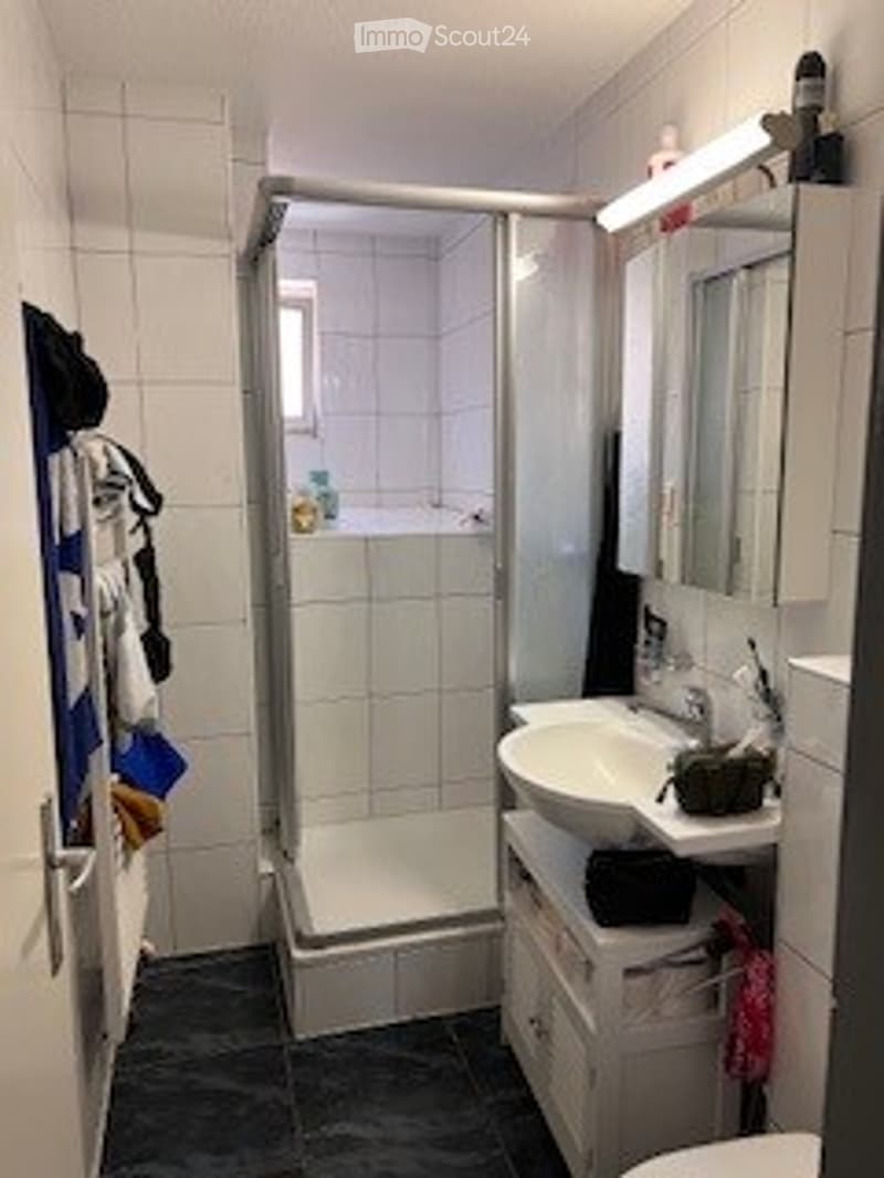 Modern bathroom with white tiles, a walk-in shower, a sink with a mirror, and a cabinet below.