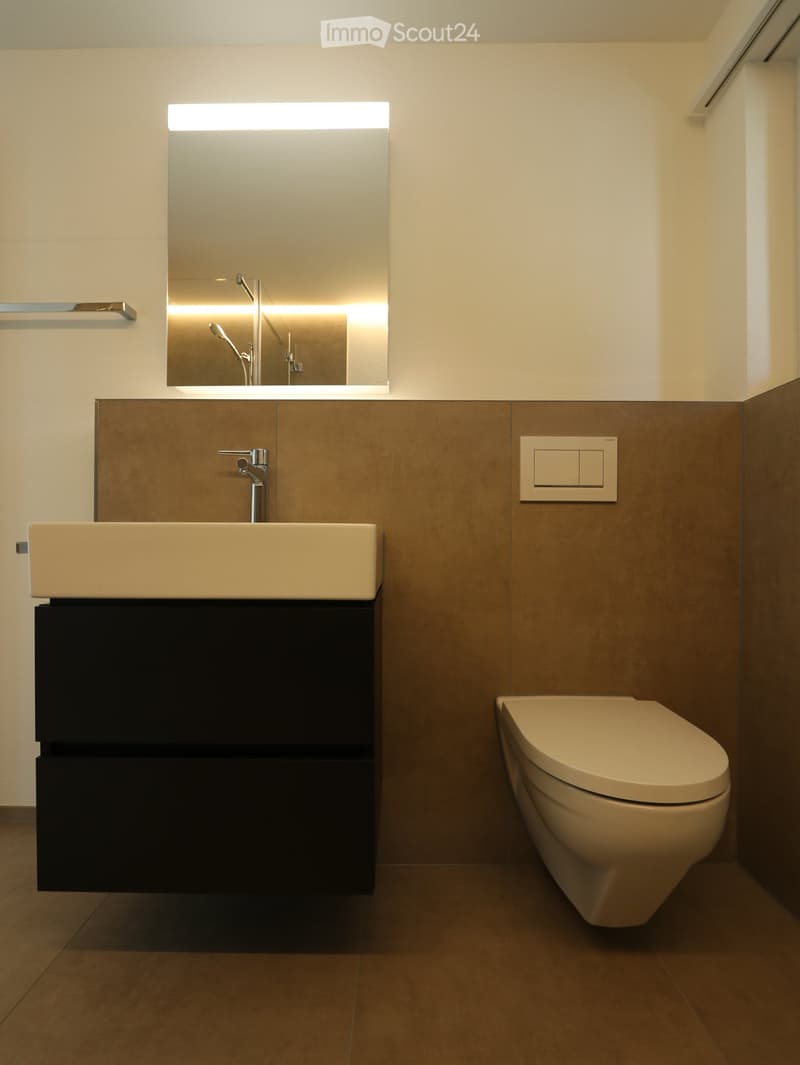 Bathroom. Modern bathroom with a beige sink, chrome faucet, large mirror, and a sleek black cabinet beneath the sink. A beige toilet is positioned to the right.