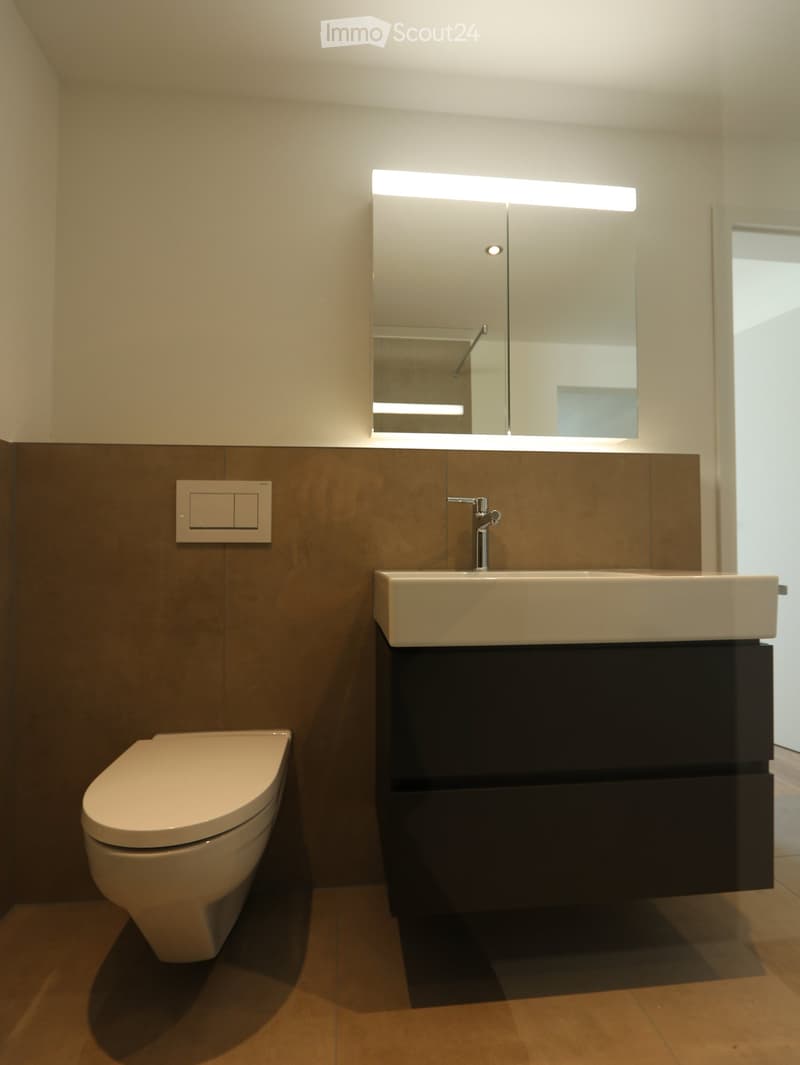 Bathroom. Modern bathroom with a white toilet, a sink with a dark wooden cabinet, a large mirror with built-in lighting, and a sleek faucet.