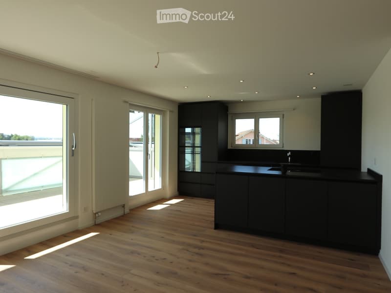 Unfurnished Room. Empty kitchen with wooden flooring, black cabinetry, and large windows offering a view of the balcony.
